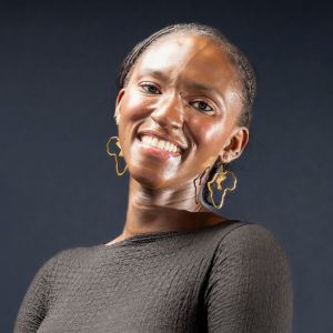 Elegant portrait of a smiling woman wearing unique Africa-shaped earrings against a dark background.