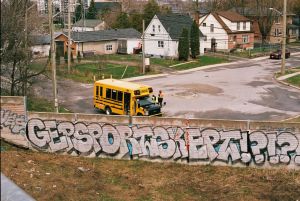 A city intersection featuring a school bus, visible graffiti, and residential homes.