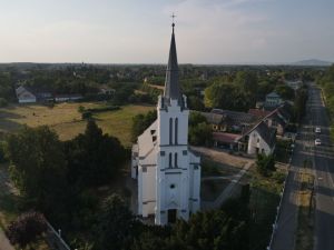 An aerial shot capturing the picturesque white church in Tiszavasvári, Hungary surrounded by lush greenery and a quaint