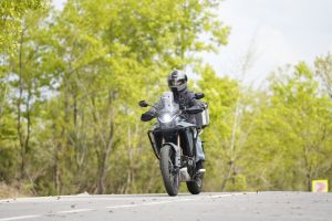 A motorcyclist in safety gear rides through a scenic forest road during daytime.