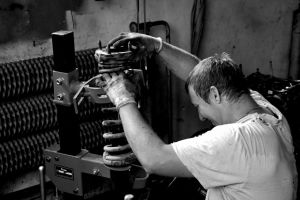 A hardworking auto mechanic in a Czech workshop adjusting a car part in black and white.