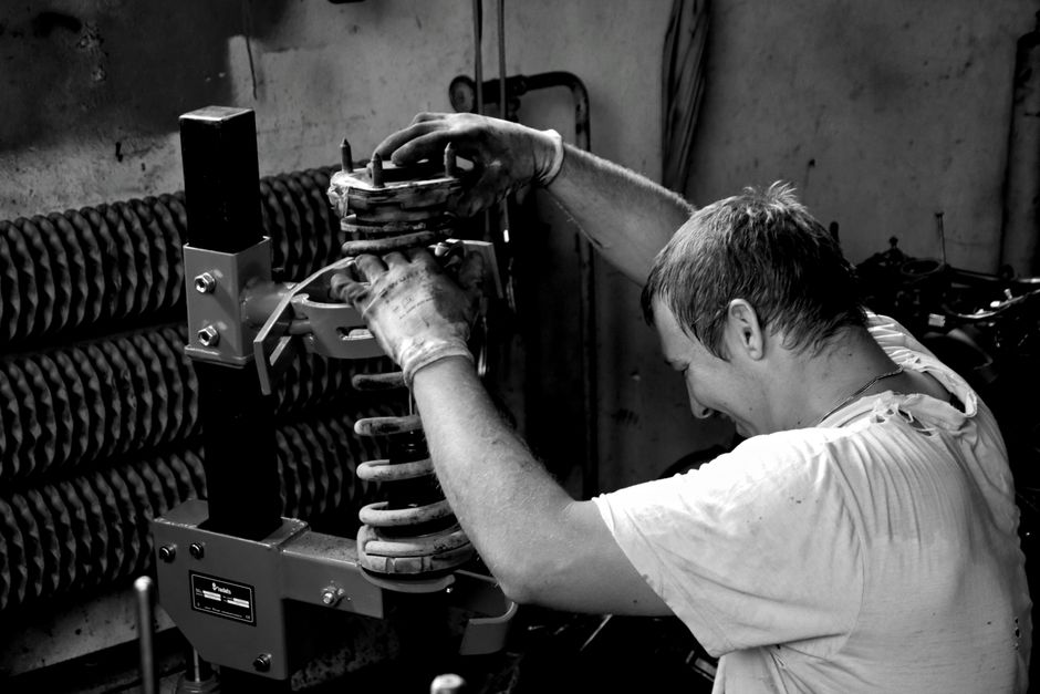 A hardworking auto mechanic in a Czech workshop adjusting a car part in black and white.