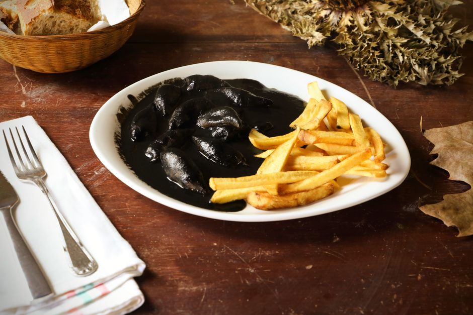 Plate of squid in ink with French fries on rustic wooden table setting.